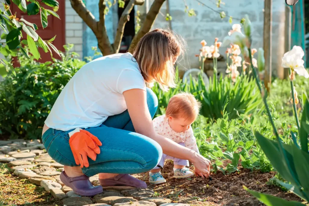 Frau und Kind hocken vor einem Beet im Garten und zupfen Unkraut.