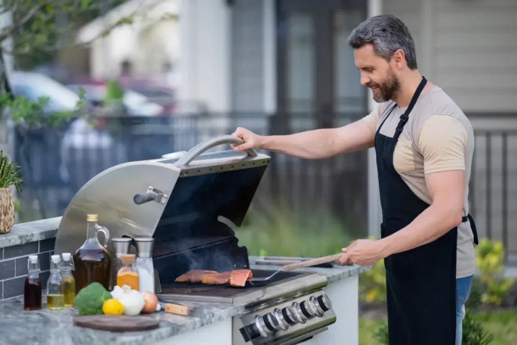Foto von einem Mann der im Garten vor seiner Outdoor-Küche steht und grillt.